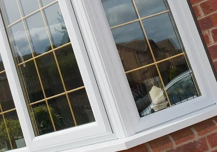 A white uPVC bay window with gold Georgian bars, seen close up against red brick